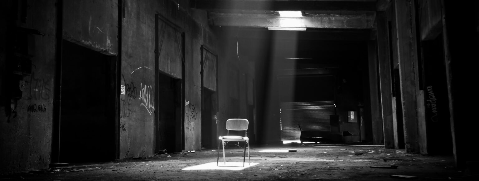 A dark warehouse with a chair being illuminated from above